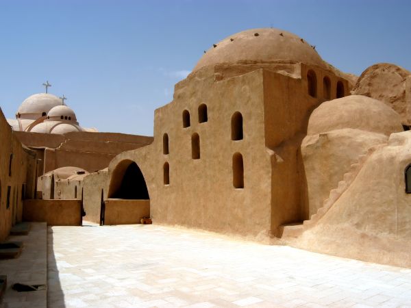 ancient monastery in the desert with palm trees and mountain backdrop