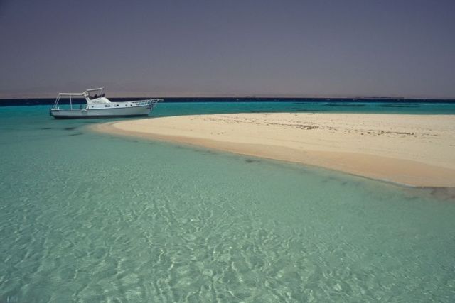 crystal clear turquoise water with a white sand island and a boat anchored nearby