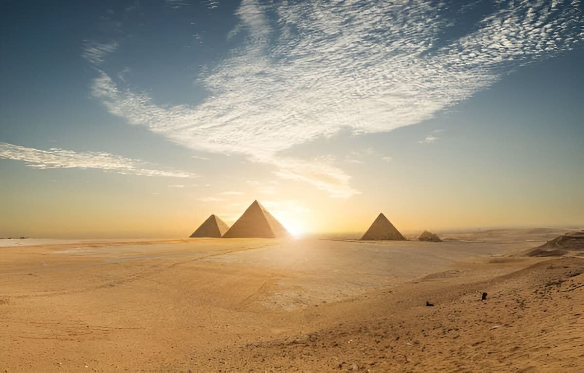 View of the pyramids standing in the middle of the Egyptian desert under a clear sky, with sand dunes in the foreground.