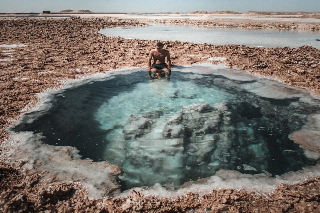 Traveler sitting in natural salt pool at Siwa Oasis with clear turquoise water