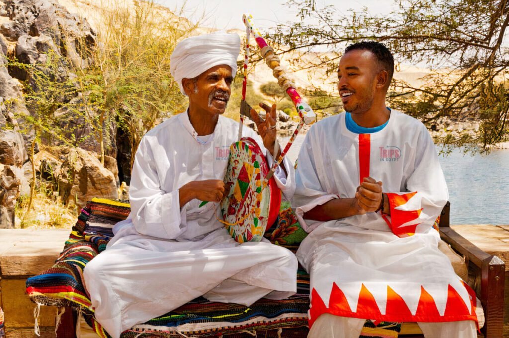 Nubian men in traditional white garments playing music and smiling by the Nile