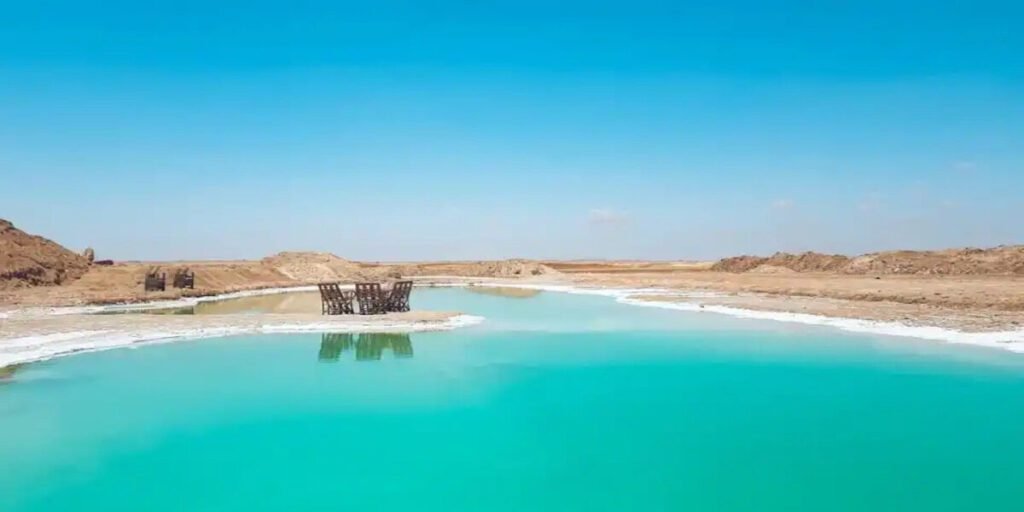 Crystal blue salt lake in Siwa Oasis with wooden chairs on the shore