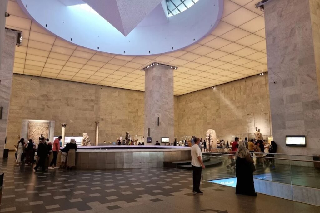 Museum exhibition hall displaying ancient Egyptian statues pottery and artifacts under soft lighting