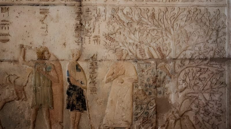 Ancient Egyptian stone wall relief depicting deities and a sacred tree with hieroglyphs